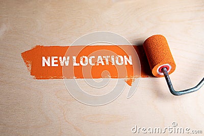 New Location. Paint roller with orange paint on a wooden surface Stock Photo