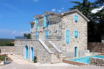 New Mediterranean villa built with stone in traditional style with blue wooden window blinds and doors next to swimming pool Stock Photo