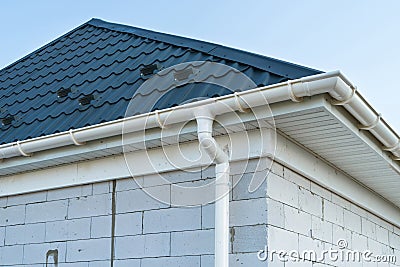 New metal tile roof with white rain gutter. SIP panel house construction. Unfinished building. Stock Photo