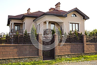 New modern luxurious expensive residential two story cottage house with shingle roof, big windows and balconies behind stone fence Stock Photo