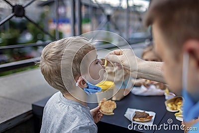 New normal reality, stay safe in street cafe, father with kids in medical masks eating fast food Stock Photo