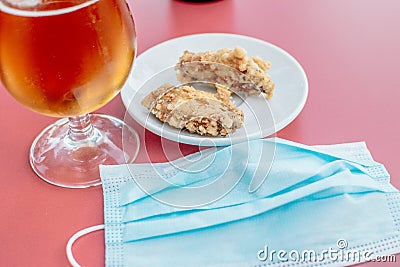 Glass of beer, plate of fried chicken wings and a face mask on a bar table Stock Photo