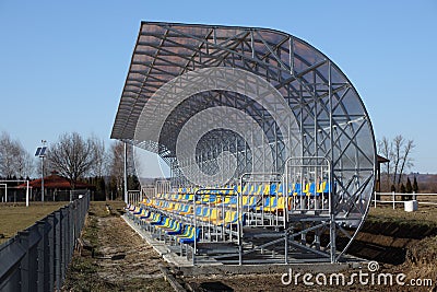 New stands on the football field of metal light construction with plastic seats in blue and yellow. Places for fans in the stadium Stock Photo