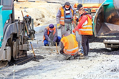 The working team of road workers in protective masks sets the necessary level for the necessary asphalting of a new section of the Editorial Stock Photo