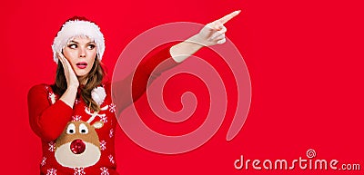 New year advertising. Christmas woman pointing finger away at copy space. Surprised girl in Santa hat. Season Sales and Stock Photo