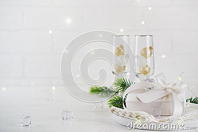 New Year Celebration. Silver Christmas table setting with two champagne glasses on the dinner table and gift box. Stock Photo