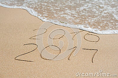 New Year 2017 is coming concept - inscription 2016 and 2017 on a beach sand, the wave is almost covering the digits 2016 Stock Photo