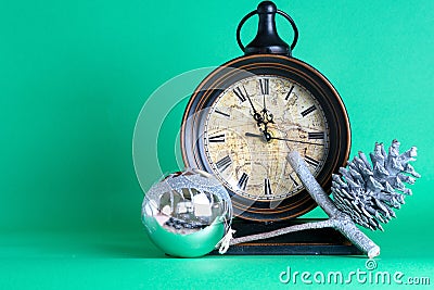 New Year`s clock midnight, bauble and cone on pine fir tree branch. Green background. Christmas greeting card. Stock Photo