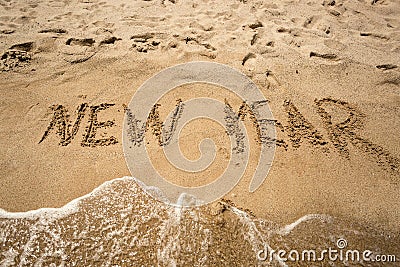 New Year written on sand and being washed by waves Stock Photo