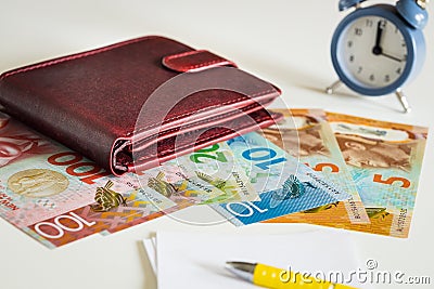 New Zealand dollars next to the wallet and the clock showing five to twelve Stock Photo