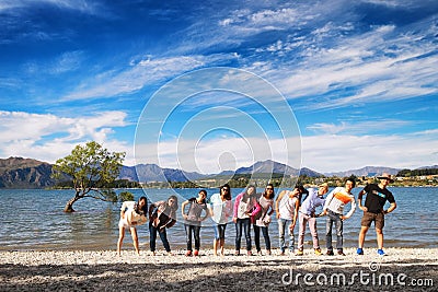 NEW ZEALAND, WANAKA - JANUARY 2016: A group of friends standing in a row in front of the famous Wanaka Tree. Wanaka is a popular Editorial Stock Photo