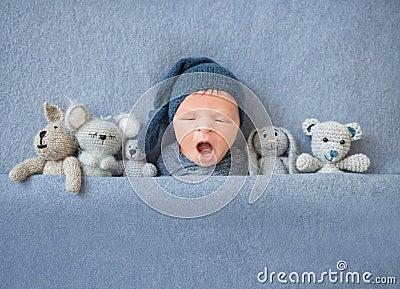 Newborn baby boy yawning and lying between plush toys Stock Photo