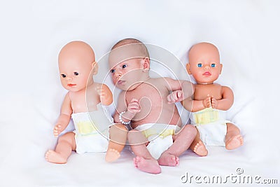 Newborn baby in diaper between two plastic dolls Stock Photo