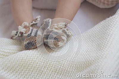 Newborn baby feet close up in wool wool brown knitted socks booties on a white blanket. The baby is in the crib. copyspace Stock Photo