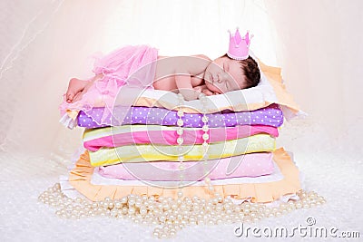 Newborn baby girl in a crown sleeping on the bed of mattresses. Fairy Princess and the Pea Stock Photo