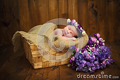 Newborn baby girl with a wreath in a wicker basket with a bouquet of purple wild flowers Stock Photo