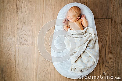 Newborn baby quietly sleeps in a special orthopedic mattress Baby cocoon, on a wooden floor. Calm and healthy sleep in newborns Stock Photo