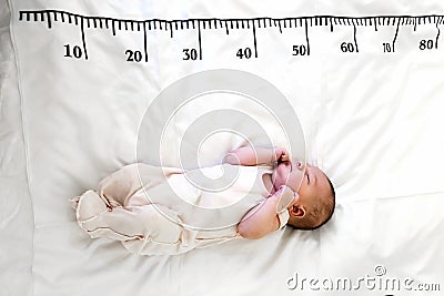 A newborn baby in white sleeps on a bed on which a measuring ruler for growth is drawn Stock Photo