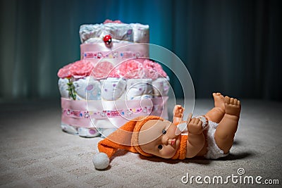 Newborn gift concept. Cake of diapers. Wrapped diapers as cake with flowers. Cake of wrapped clean diaper on table with baby doll Editorial Stock Photo