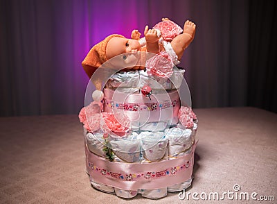 Newborn gift concept. Cake of diapers. Wrapped diapers as cake with flowers. Cake of wrapped clean diaper on table with baby doll Editorial Stock Photo