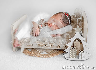 Newborn Girl Sleeping On Small Bed With Toy Deer And Tiny Christmas Tree Nearby Stock Photo