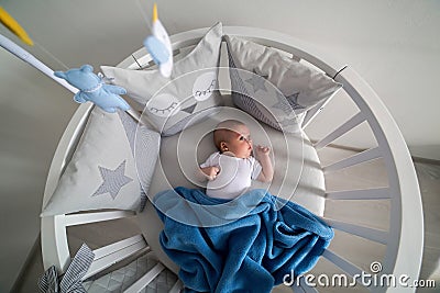 Newborn lies in the round white bed with mobile Stock Photo