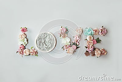 Newborn love background - word Love spelled with flowers and round bowl on light grey background Stock Photo