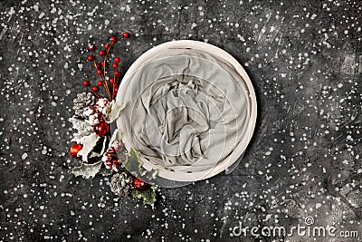 Newborn winter background - round cream bowl with CHristmas red berries and snow covered branches garland on dark backdrop Stock Photo