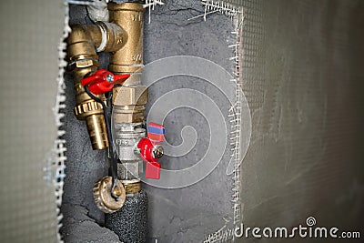 Newly installed brass water pipes plumbing with red tap fittings, gray cement wall reinforced with plastic mesh around, closeup Stock Photo