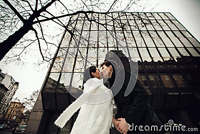 Newlyweds kiss under a huge glass building Stock Photo