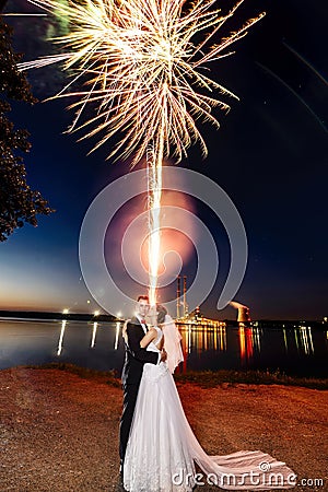 Newlyweds kissing near lake by night - fireworks Stock Photo