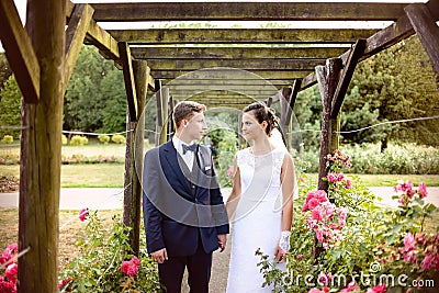 Newlyweds in park rosarium next to beautiful pink roses Stock Photo