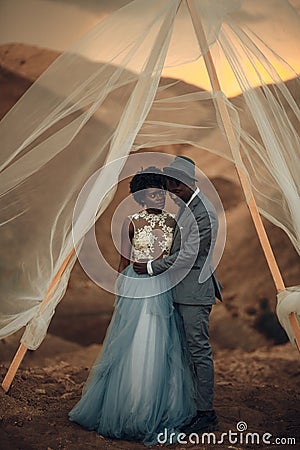 Newlyweds stand and embrace under wedding tent in canyon at sunset. Stock Photo