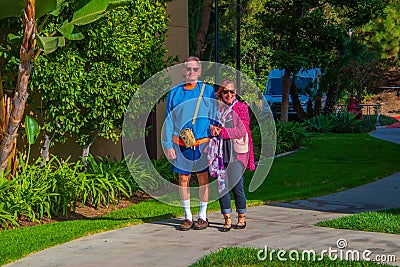 Senior citizen male caucasian baby boomer with Alzheimer`s Disease wearing shorts and high white athletic socks being helped to Editorial Stock Photo