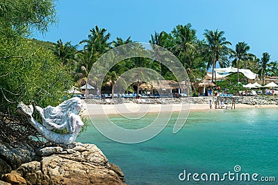 NHA TRANG, VIETNAM - APRIL 19, 2019: Sculpture of a mermaid on the beach and thatched houses on the sand in the tropics Editorial Stock Photo