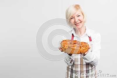 Nice and awesome picture of smiling grandma that baked a tasty pie. She holds the pie in ger hands and want it to share Stock Photo