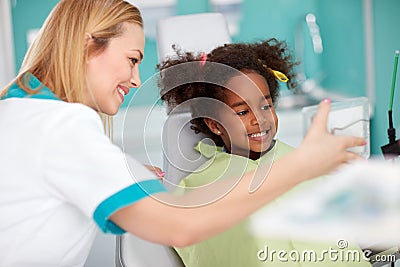 Nice black girl in dental chair showing teeth in mirror to dental assistant Stock Photo
