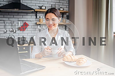 Nice cheerful businesswoman sit at table in kitchen and look at laptop. She works at home. Model hold white cup with Stock Photo