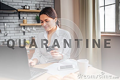 Nice cheerful woman sit at table in kitchen. She work at home. Woman hold black credit card nd type on laptop keyboard Stock Photo