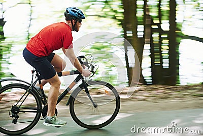 Nice feeling. Cyclist on a bike is on the asphalt road in the forest at sunny day Stock Photo
