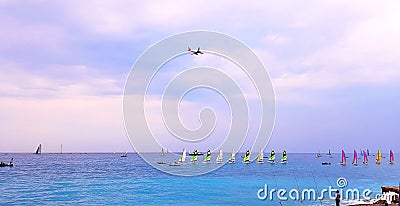 NICE, FRANCE - MAY 2018: Beach at sunset, colorful sailboats in the sea, airplane flying over the sea, Cote d`Azur, France Editorial Stock Photo