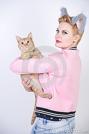 Nice kind woman with a short haircut and fur ears in sports clothes and jeans is holding her beloved pet on a white background in Stock Photo