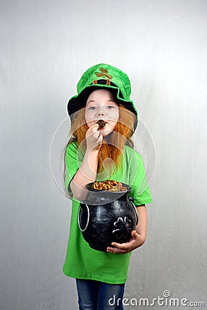 Nice littel girl with decorative red beard in green dress and leprechaun's hat, kissing golden coin with four-petal shamrock Stock Photo