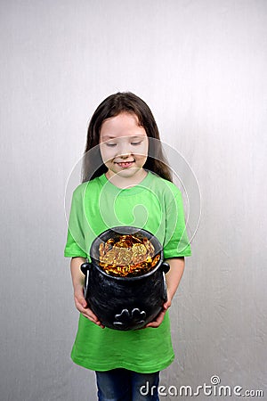 Nice littel girl in green dress looking at leprechaun's gold treasure in cast iron pot decorated by clover leaf Stock Photo