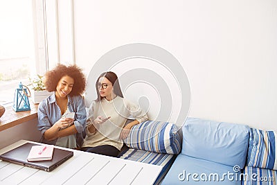 Nice picture of students sitting close to each other on sofa. THey are holding phones in their hands. Afro american girl Stock Photo