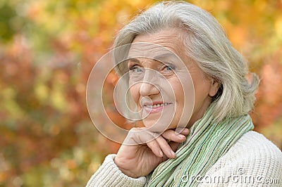 Portrait of nice smiling senior woman posing on blurred autumnal background Stock Photo