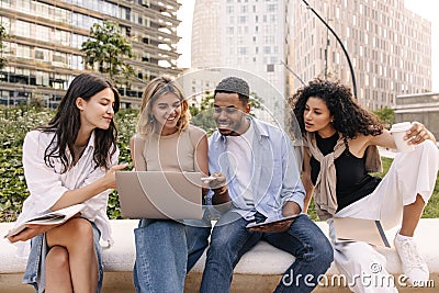 Nice young interracial students looking at laptop screen browsing presentation sitting outside. Stock Photo
