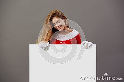 Nice young mrs.Santa Claus dressed in the red robe and white gloves holds the white canvas in front of her on the gray Stock Photo