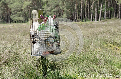 A metal litter bin full with rubbish on a wooden post in the countryside Editorial Stock Photo