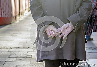 Elderly persons wrinkled hands held behing their back while walking Editorial Stock Photo